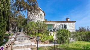 A stone building with a circular tower, a stone staircase, and a garden with a table and chairs. - VILLA JUSTINE VI4239 By Riviera Holiday Homes (Mandelieu-la-Napoule)
