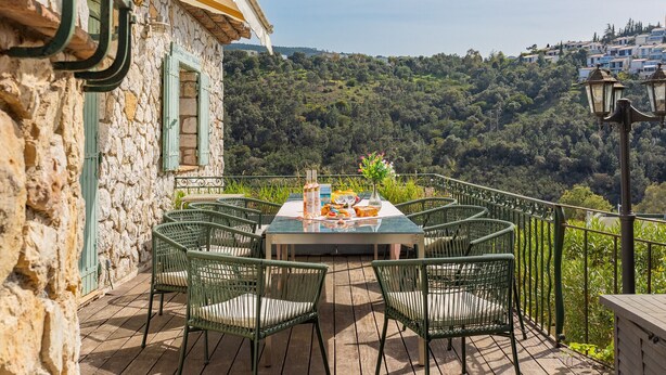 Une terrasse avec une table dressée pour le repas, entourée de chaises, et offrant une vue sur une colline verdoyante.
