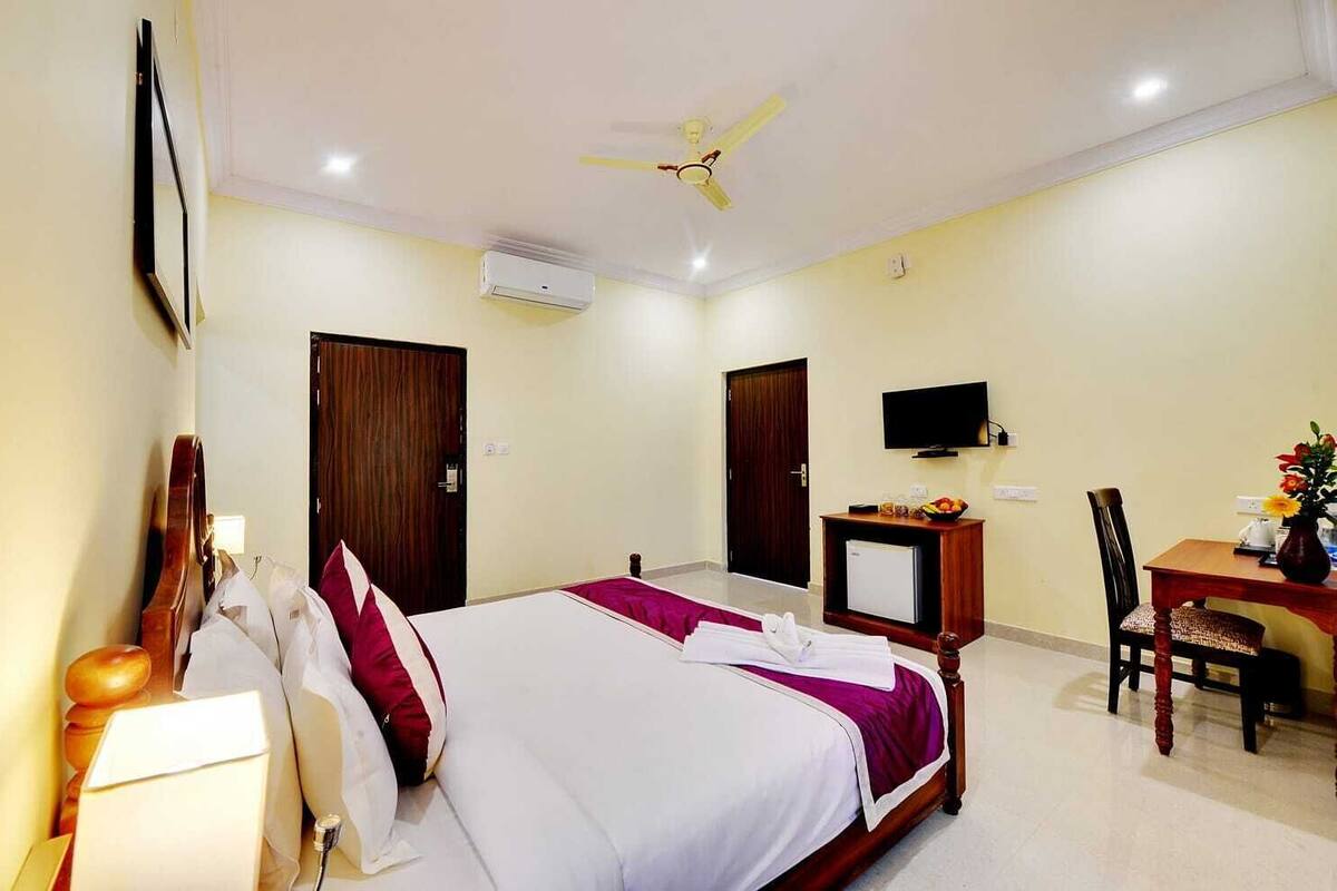 A hotel room with a bed, a desk with a chair, a television, and a ceiling fan.