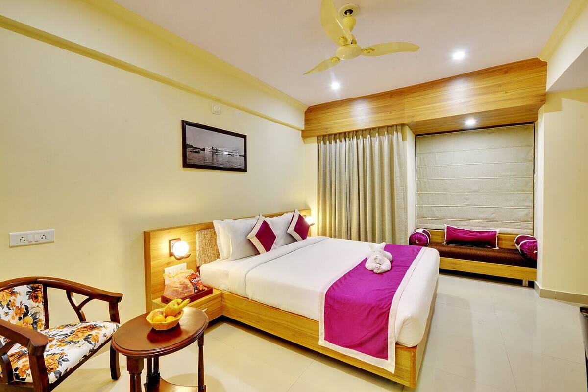 A hotel room with a bed, a desk with a chair, a ceiling fan, and a window with curtains.