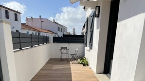Una terraza de madera con una pequeña mesa y una silla, rodeada de paredes blancas y una barandilla negra.