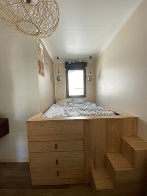 Une chambre à coucher de taille réduite, dotée d’un lit intégré, de tiroirs en bois et d’un plafond en pente.