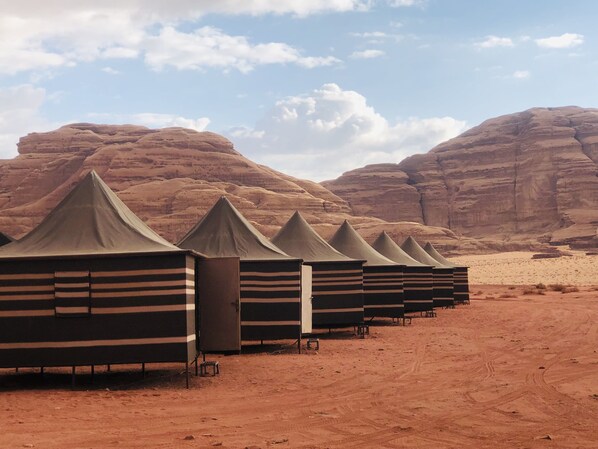 A row of tents in a desert with rocky hills in the background.