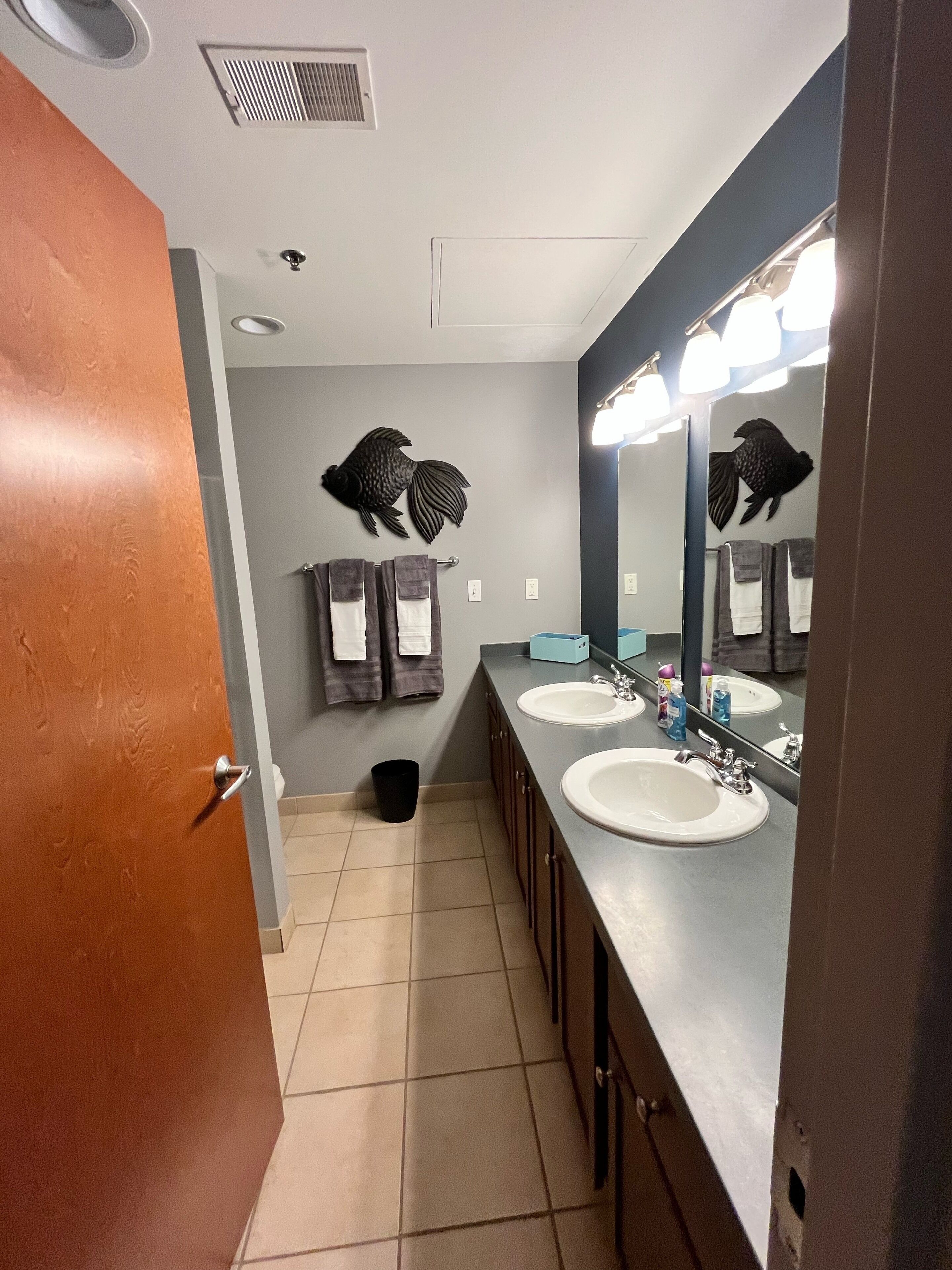 A bathroom with two sinks, a large mirror, and decorative fish wall art.