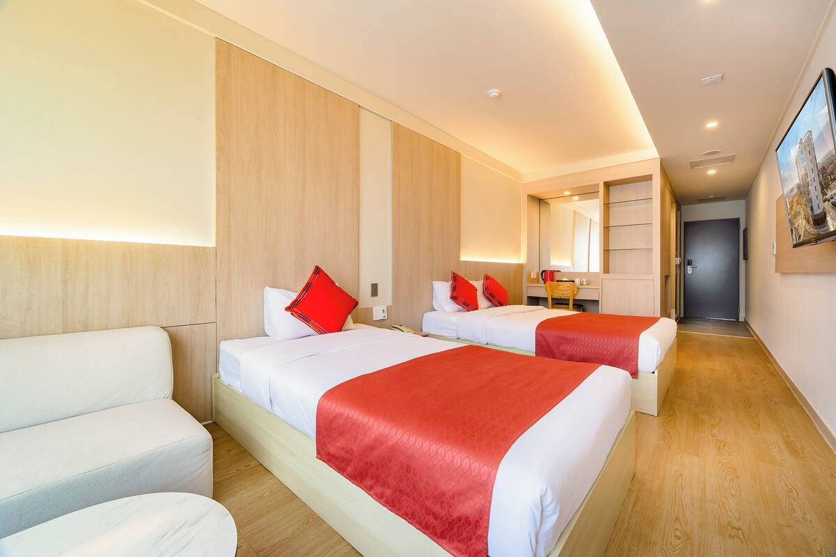 A hotel room with three beds, a sofa, a desk, and a mirror.