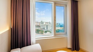 Una sala moderna con un sofá y una mesa de centro, un ventanal con cortinas y vistas a edificios y un cielo despejado.