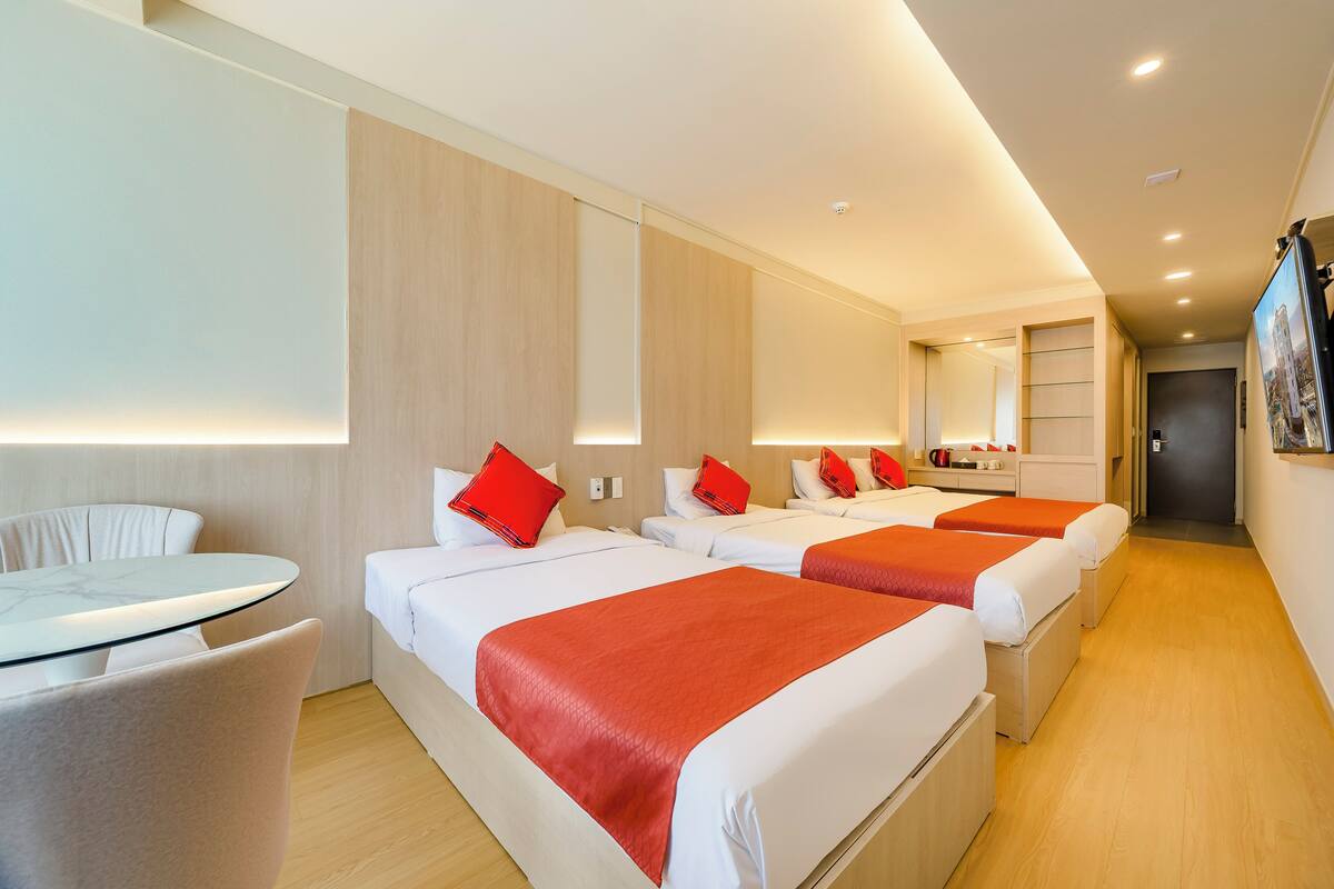 A hotel room with three beds, a small table, and a chair.