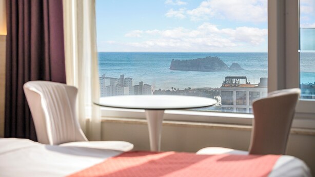 Habitación de hotel con vista al mar y un promontorio rocoso distante.