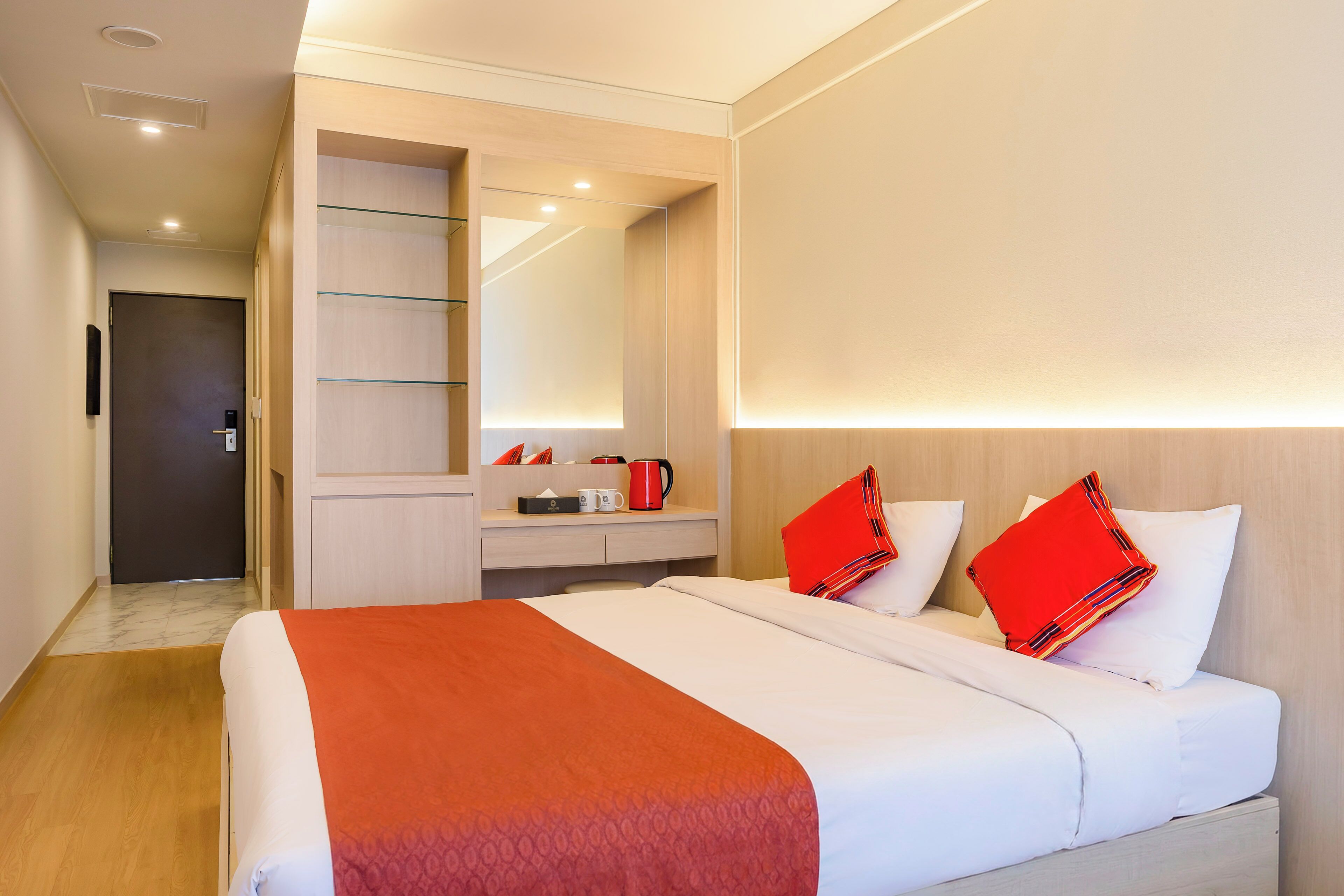 Quarto de hotel com uma cama, mesa de cabeceira, espelho e porta.