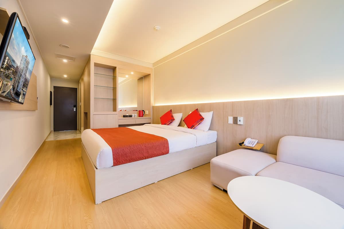 A modern hotel room with a bed, a sofa, a bedside table with a phone, and a large mirror.