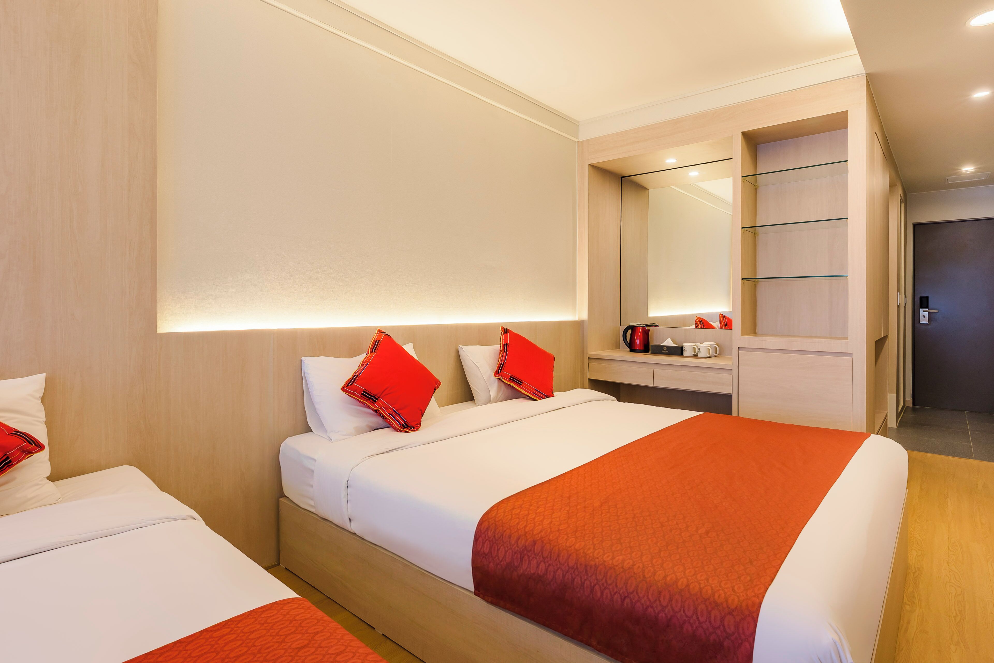 Una camera d'albergo con due letti, un ampio specchio, un minibar e una porta.
