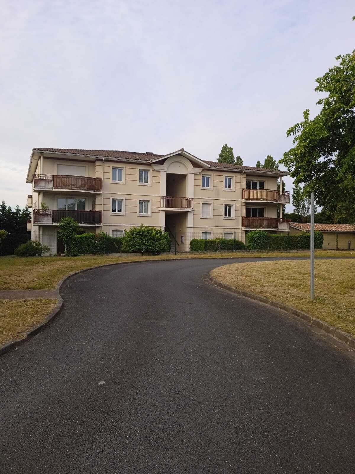 A multi-story residential building with a central entrance, balconies, and a surrounding grassy area.