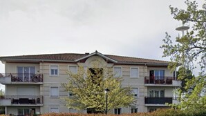 Un immeuble résidentiel à plusieurs étages, doté de balcons, d’une entrée principale et d’une haie bien entretenue à l’avant.
