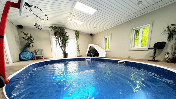 Een binnenzwembad met helderblauw water, een rode poolladder en een plafondventilator.