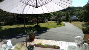 Eine Terrasse mit weißem Sonnenschirm, Kübelpflanzen und einer Statue.