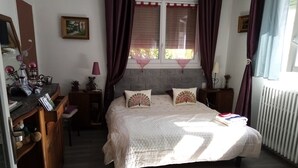 Ein Schlafzimmer mit Bett, Schreibtisch, Kommode und einem Fenster mit Vorhängen.