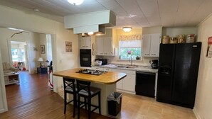 A kitchen with a wooden island, black refrigerator, white cabinets, and a window with blinds. - Charming 1930's house only a few blocks from the St. Johns River! (Welaka)