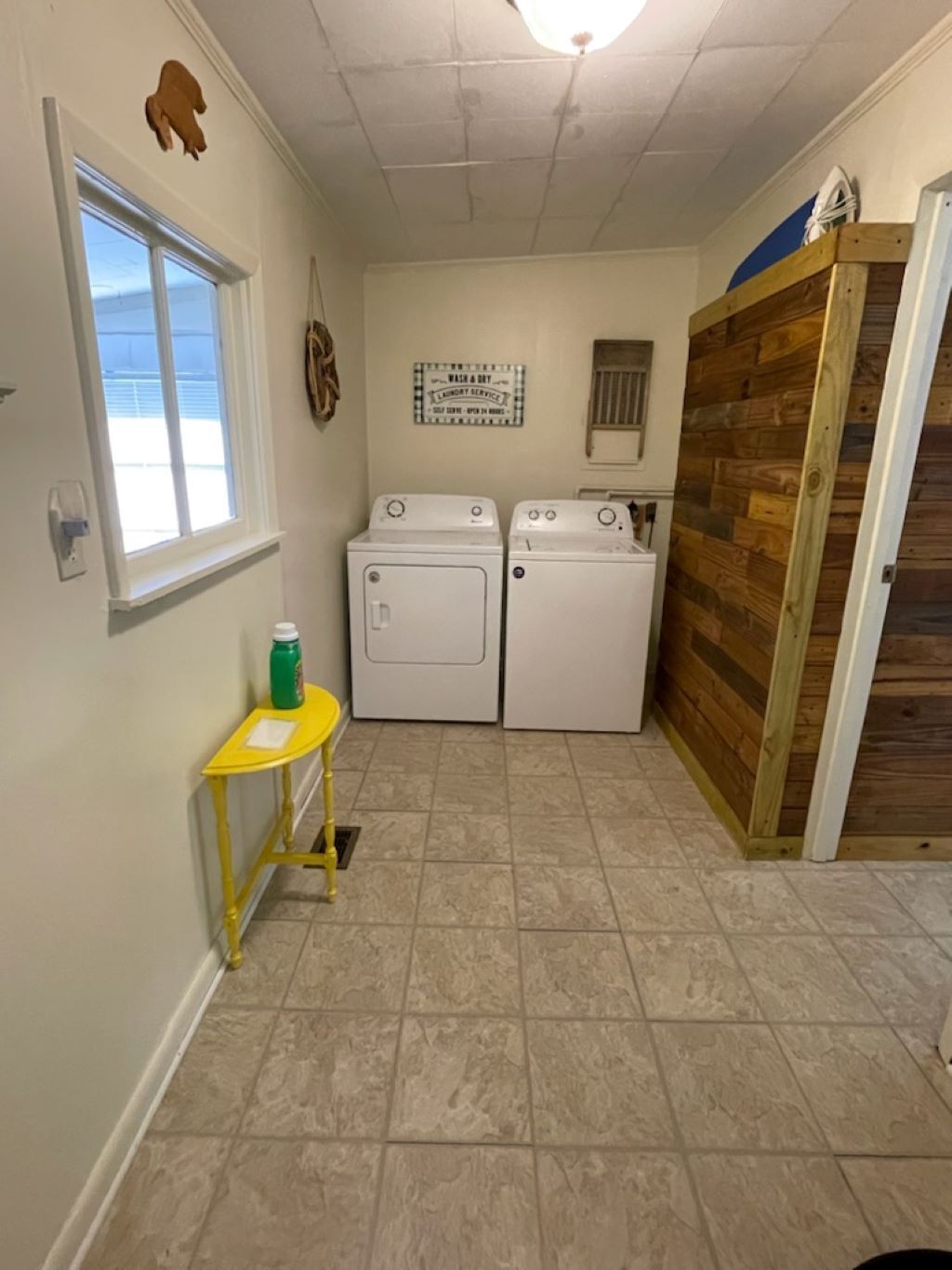 A laundry room with two washing machines, a small table with a bottle, and a wooden door.