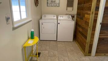 A laundry room with two washing machines, a small table with a bottle, and a wooden door.