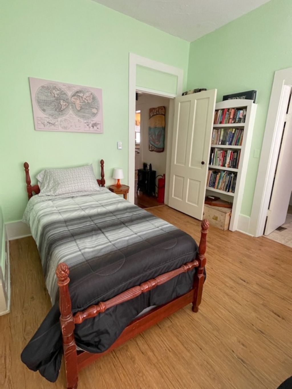 Un dormitorio con una cama de madera, una estantería y una puerta que da a otra habitación.