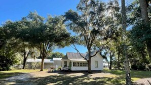 A white house with a porch, surrounded by trees and a grassy yard. - Charming 1930's house only a few blocks from the St. Johns River! (Welaka)