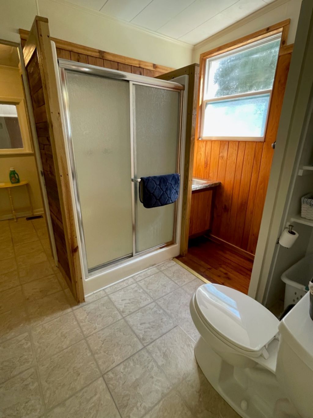 A bathroom with a shower, toilet, and a window.