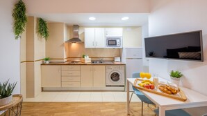 Une cuisine compacte équipée d’un four à micro-ondes, d’un four et d’un lave-linge. Un coin repas avec une table préparée pour le petit-déjeuner est également à disposition.