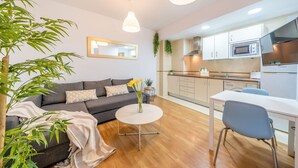 Un espace de vie compact comprenant un canapé, une petite table ronde, un coin cuisine équipé d’appareils modernes et une table à manger avec des chaises.