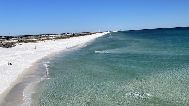 A beach with clear shallow waters, a sandy shore, and a distant pier. - Family Friendly with Gameroom! Outdoor swings and more! (Navarre)