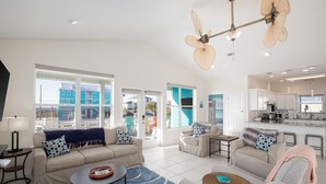 A spacious living room with a sofa, armchairs, and a coffee table. There are large windows offering a view of the outside. - Family Friendly with Gameroom! Outdoor swings and more! (Navarre)