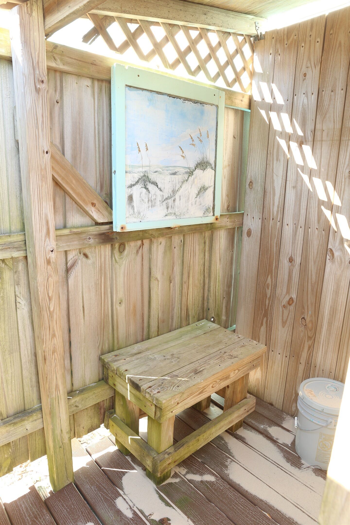 A wooden deck with a bench and a painting of a beach scene.