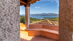A stone pillar, a wooden pergola, and a terracotta bench overlooking a coastal landscape with mountains. - Villette Coda Cavallo (San Teodoro)
