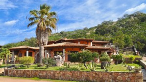 A multi-story building with a tiled roof, surrounded by a stone wall and various plants. - Villette Coda Cavallo (San Teodoro)