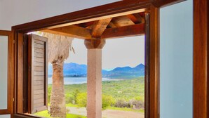 A window with a view of a mountainous landscape, a palm tree, and a wooden structure. - Villette Coda Cavallo (San Teodoro)