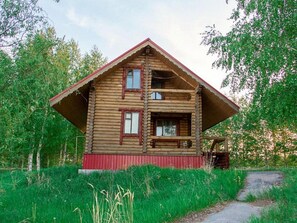 A wooden log cabin with a red roof and two visible windows.