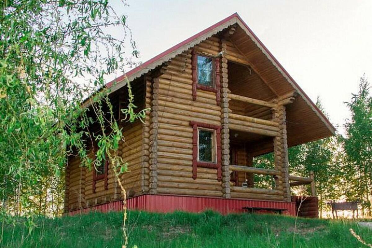Una cabaña de troncos con estructura de dos pisos, un porche y techo rojo.