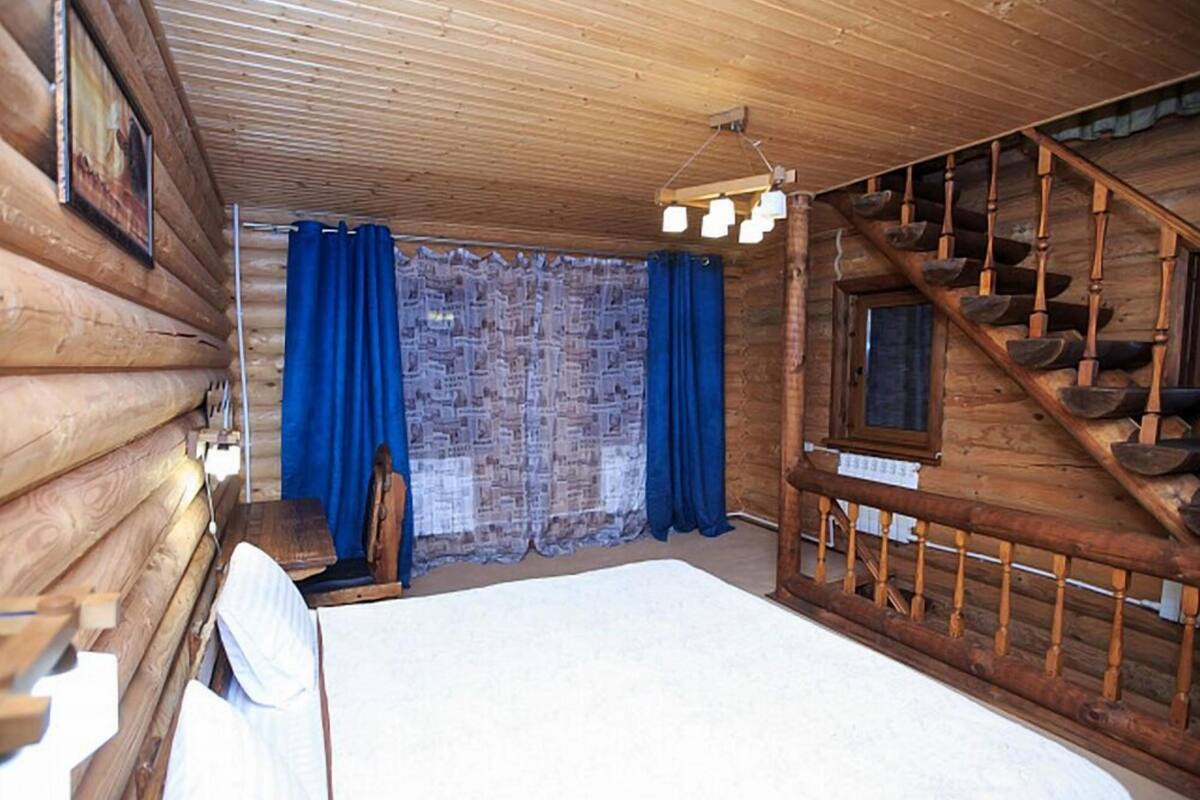 Una habitación tipo cabaña de madera con una cama, una escalera de madera y una ventana cubierta con cortinas.