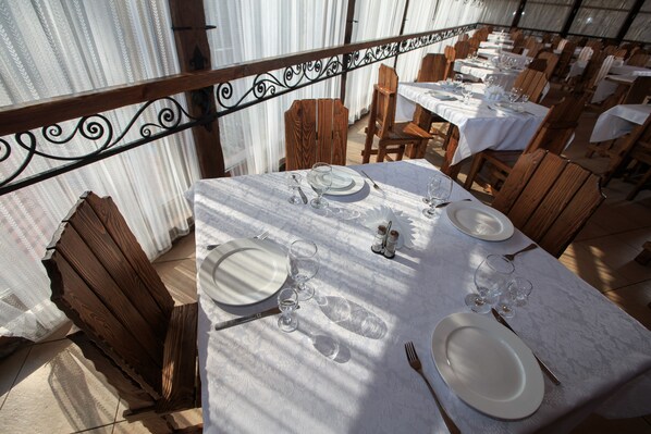 A dining area with tables set for a meal, featuring white tablecloths and wooden chairs.