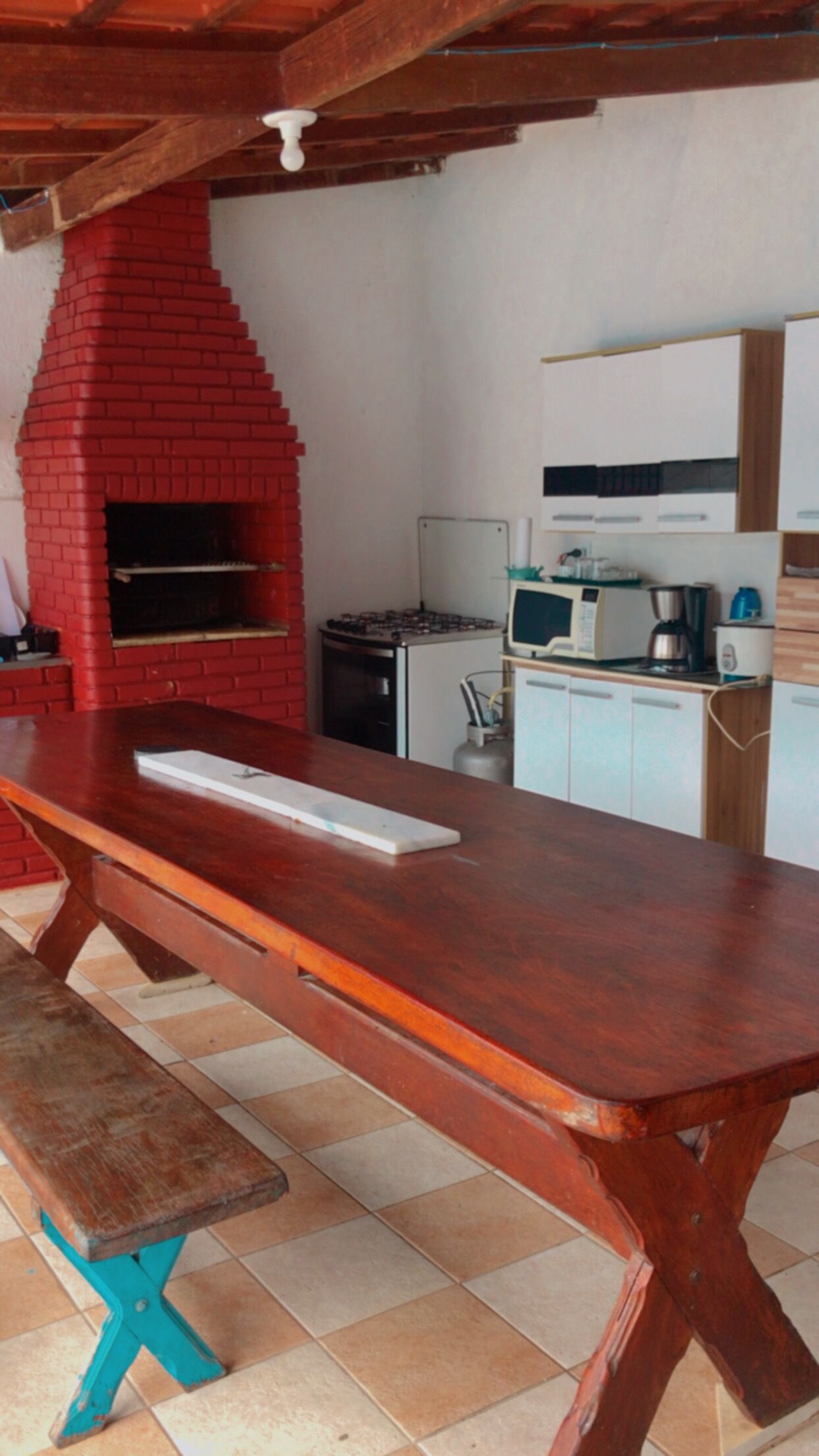 A kitchen with a red brick oven, a wooden table, and a tiled floor.