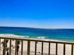 Ein Strand mit klarem, blauem Wasser, einem Sandufer und einem Geländer im Vordergrund.