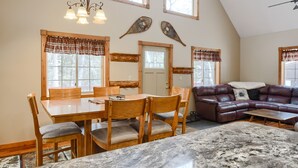 A dining area with a wooden table and chairs, a leather sofa, and a large window with plaid curtains. - 3-Level Spacious Cabin w/ Pool Table, Foosball, Close to Terry Peak & Skiing (Lead)