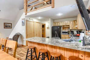 A kitchen with wooden cabinets, a granite countertop, and a built-in sink. There are three stools and a chair in the dining area. - 3-Level Spacious Cabin w/ Pool Table, Foosball, Close to Terry Peak & Skiing (Lead)