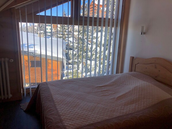 A bedroom with a bed, a window with blinds, and a view of a snowy landscape.