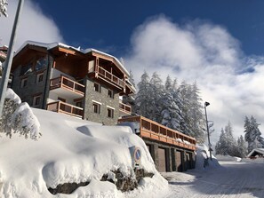 A multi-story hotel with balconies, surrounded by snow-covered trees and a clear sky.