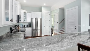 A modern kitchen with white cabinets, a stainless steel refrigerator, and a marble countertop. - Pet Friendly Gulf View Townhome | Sleeps 10 | Game Room (Pensacola Beach)