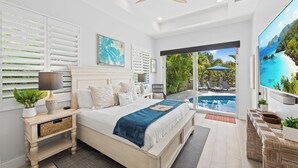 A bedroom with a bed, bedside tables, a nightstand, a ceiling fan, a large window, and a view of an outdoor pool area.