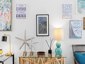 Ein Zimmer mit Glastisch, Holzeinrichtung, einer Skulptur einer Seeanemone und Wandbildern mit Strandmotiv.