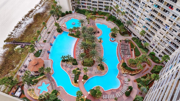 A high-rise hotel with a large central swimming pool surrounded by palm trees and sun loungers. - Beach Front Free round of Golf & Activities Daily! (Panama City Beach)