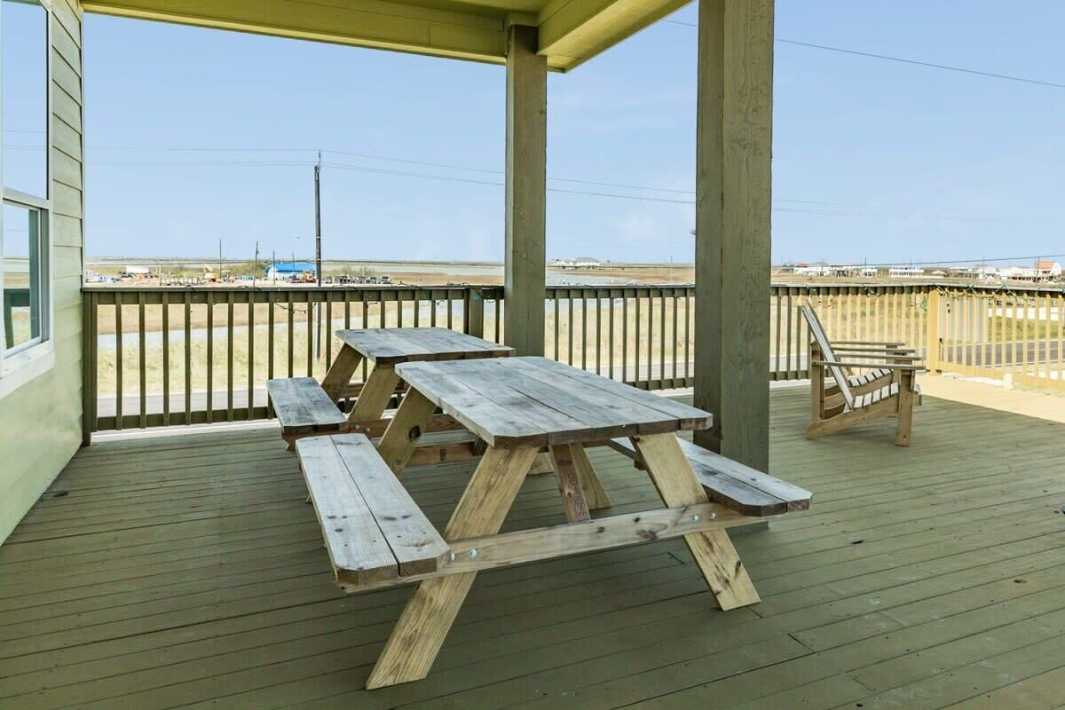 A wooden deck with picnic tables and a chair, overlooking a flat landscape.