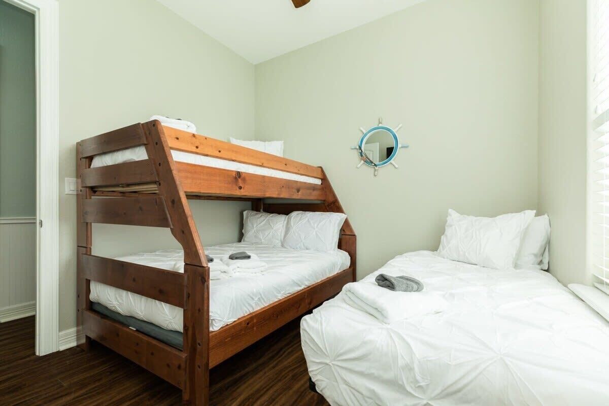 Une chambre avec un lit superposé en bois et un lit simple. Un miroir rond est accroché au mur.